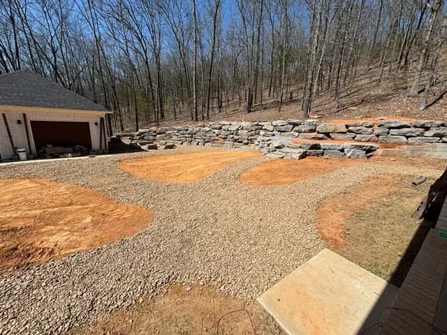 Dirt Work Innovations — Central Arkansas Finished gravel yard with planting beds below a stone retaining wall in Central Arkansas